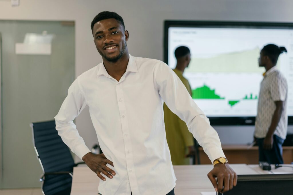 Smiling business professional in white shirt in an office with colleagues working in background.